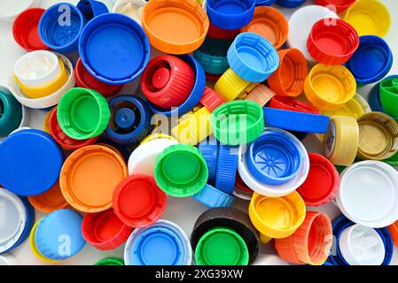 Multi-colored plastic caps from plastic bottles lie on a white wooden table in a pile Stock Photo