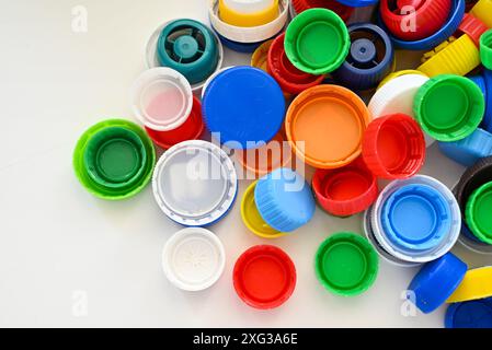 Multi-colored caps from plastic bottles lie on a white wooden table in a chaotic order Stock Photo