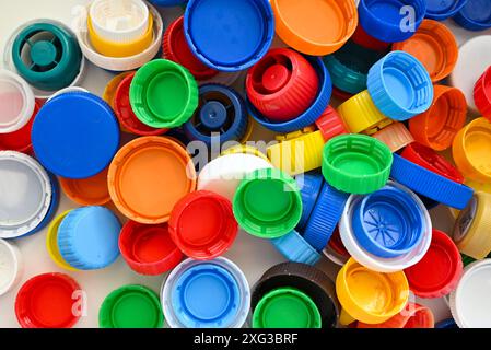 Multi-colored plastic caps from plastic bottles are scattered on a white wooden table in a pile Stock Photo