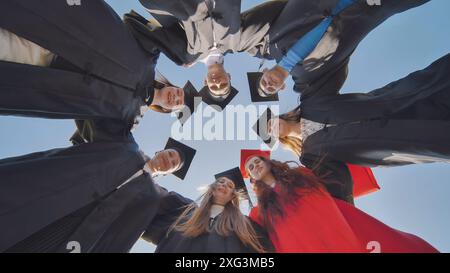 College graduates in a circle stand hugging each other. Stock Photo