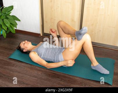 Shot of the woman performing various stretching and physical exercises laying on the yoga mat on the floor Stock Photo