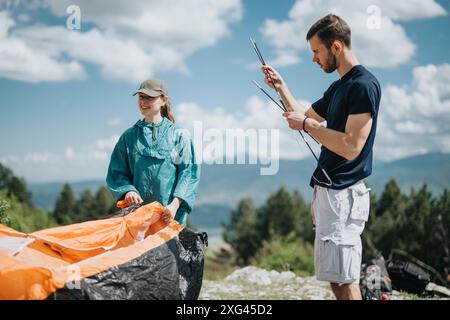 Happy couple setting up a tent on a sunny day in the mountains. Stock Photo