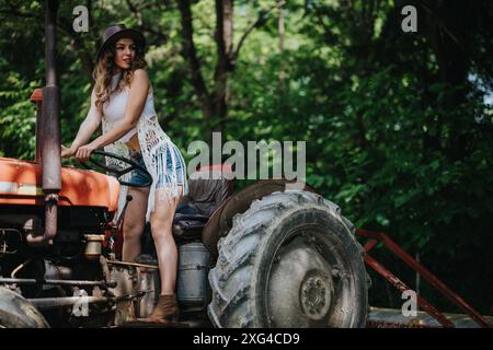 Young woman in casual summer outfit posing on a vintage tractor in a lush forest setting Stock Photo