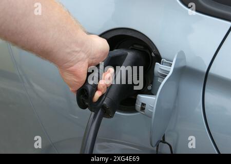 Man inserting plug into electric car socket at charging station outdoors, closeup Stock Photo