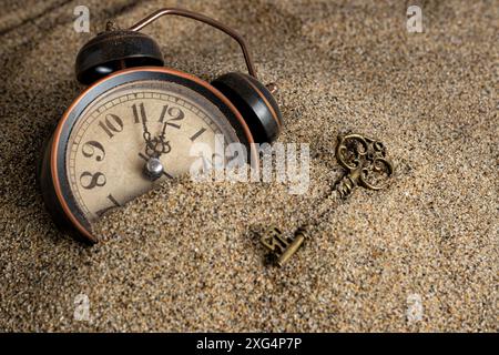 Vintage alarm clock and key in sand. Time management concept Stock Photo