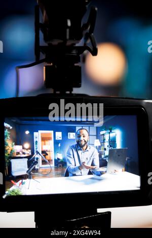 Focus on professional video production gear used for capturing footage of cheerful internet star in blurry background filming tech reviews for niche viewership, showcasing gaming laptop Stock Photo