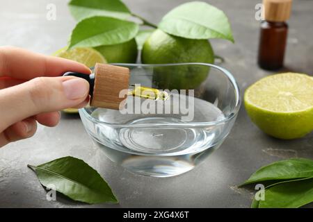 Woman dripping essential oil from pipette into bowl at gray table, closeup Stock Photo