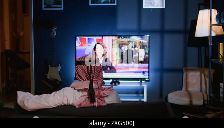Arabic man lounged on comfortable sofa, watching news broadcast while relaxing in apartment after hard day at work. Middle Eastern person loafing on couch, looking at TV channel showing current events Stock Photo