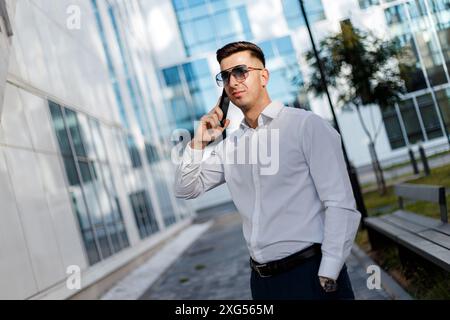 A man standing outside a building engaged in a phone conversation. He holds a cell phone to his ear, gesturing while talking. Stock Photo