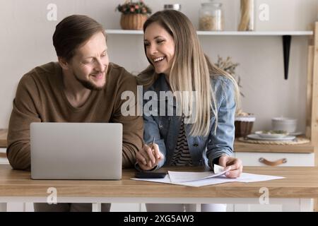 Smiling spouses do paperwork in home kitchen use laptop Stock Photo