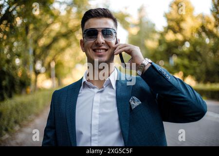 A man dressed in a formal suit and wearing sunglasses is engaged in a phone conversation. Stock Photo