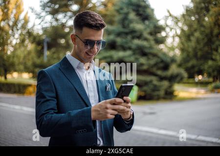 A man dressed in a formal suit is focused on his cell phone screen, seemingly engrossed in the information displayed. Stock Photo