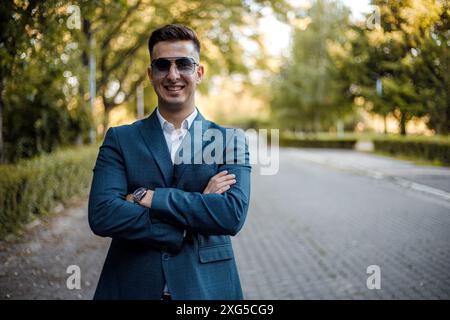 A man dressed in a suit and sunglasses stands confidently in the center of a road, appearing focused and in control of his surroundings. Stock Photo