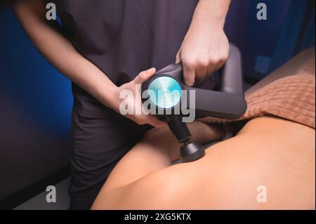 Percussive massager, sports man getting his back massaged to relieve pain, top side view close-up Stock Photo