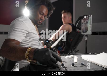 Professional African American tattoo artist makes a tattoo on client arm. High quality photography Stock Photo