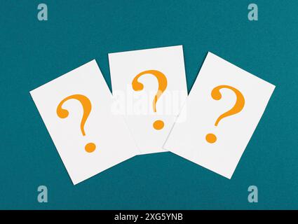 Three orange colored question marks on paper, petrol background, looking for an answer, searching for knowledge, problem solving concept Stock Photo