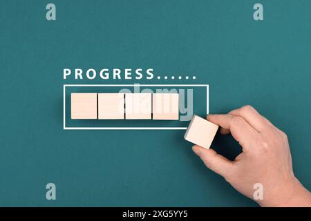 The words progress is standing over the loading bar, hand puts last cube to the upload, petrol colored background Stock Photo