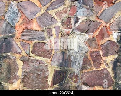 Wall consisting of irregularly shaped stones in different colours, including red, orange, grey and brown. The stones are connected with mortar, which Stock Photo