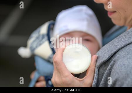 Close-up of a baby being fed from a bottle by the mother, dressed in a gray coat. The baby is warmly dressed in a knitted hat and jacket Stock Photo