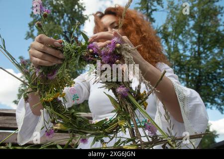 Moscow, Russia. 6th of July, 2024. A woman weaves wreaths of wildflowers during a celebration of the Belarusian holiday 'Kupalle' in Ostankino Park in Moscow, Russia. Kupalle or Ivana Kupala Day, also known as Ivana-Kupala or Kupala Night, is a traditional pagan holiday folk celebration in eastern Slavic cultures. Girls create and wear flower wreaths and perform various rituals. Initially, Ivana-Kupala was a pagan fertility rite that was also connected to the celebration of the summer solstice when nights are the shortest Stock Photo