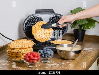 Making Belgian waffles. Female hand pours dough into waffle maker in kitchen at home. Cooking summer breakfast with round waffles and berries Stock Photo