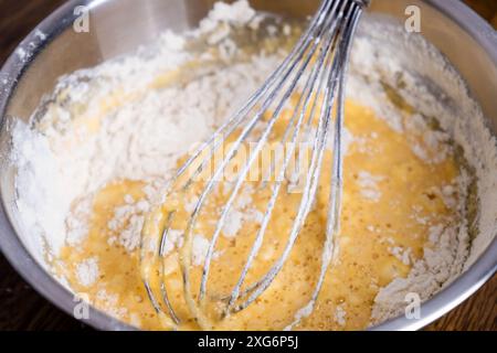 Bowl of batter and whisk on wooden table. Close-up of mixing dough for bakery and cooking. Ingredients for waffles, cakes or pancakes. Dough Stock Photo