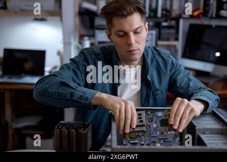 Young caucasian man disassembles broken computer. Computer service and repair concept. Computer disassembling in repair shop, workshop. Electronic dev Stock Photo