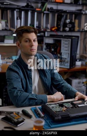 professional confident repairman or technician repairs computers and laptop. portrait of service engineer in shirt repairing a laptop, looking at came Stock Photo