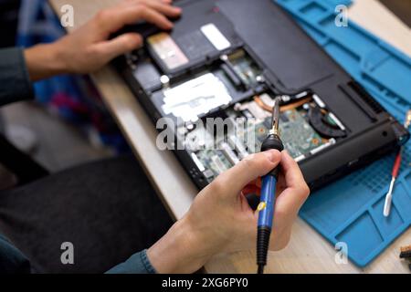 cropped male hands repairing parts in disassembled laptop using screwdriver and different tools on table in workshop. Hand technician repairing broken Stock Photo
