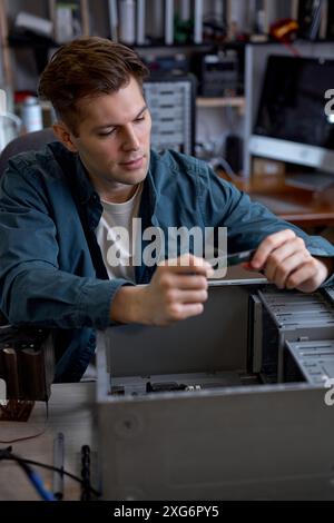 Young caucasian man disassembles broken computer. Computer service and repair concept. Computer disassembling in repair shop, workshop. Electronic dev Stock Photo