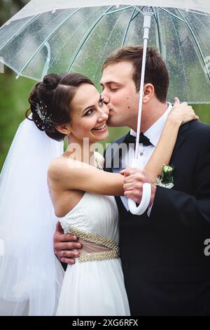 bride and groom on a rainy wedding day walking under an umbrella Stock Photo