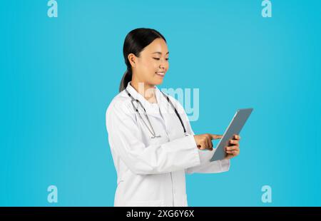 Woman Doctor in White Coat Using Digital Tablet Against Blue Stock Photo