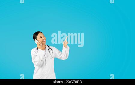 Smiling Woman Doctor Talking On Phone And Pointing Upwards Stock Photo