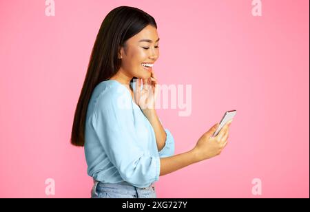 Smiling Woman Using Smartphone Against Pink Background Stock Photo