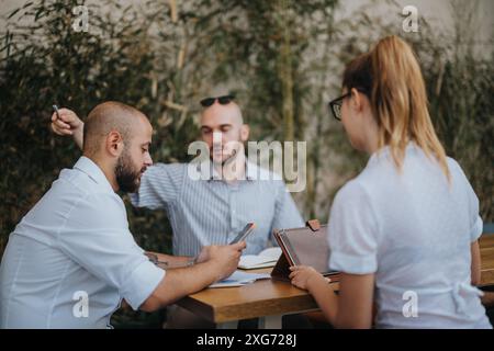Outdoor business meeting with three colleagues discussing ideas and planning over digital devices Stock Photo