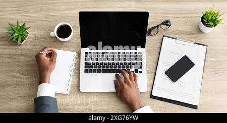 Person Working on Laptop and Taking Notes at Desk Stock Photo