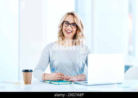 Portrait, business woman and writing notes on laptop in startup for creative project, data or stats. Face, smile and social media manager in glasses Stock Photo