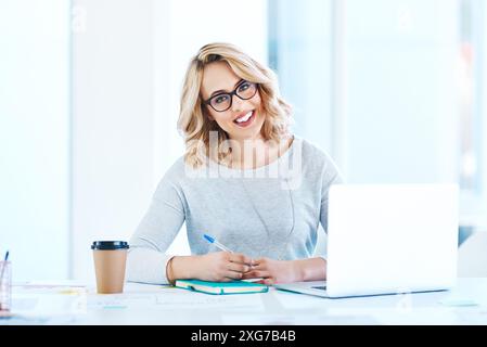Portrait, creative and business woman writing notes on laptop for project, data or stats in startup. Face, smile or social media manager in glasses Stock Photo