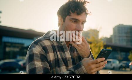 Caucasian man happy surprised face businessman using smartphone outdoors sun sunlight shocked guy shock emotion wonder amazing astonishment in city Stock Photo
