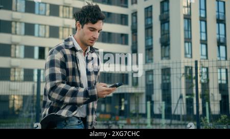 Caucasian 30s business man smiling happy guy millennial walking with mobile phone in city satisfied cheerful businessman male using smartphone app Stock Photo