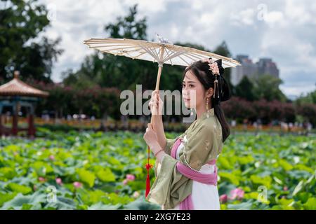 Kunming, China's Yunnan Province. 7th July, 2024. A woman enjoys lotus flowers at Daguan Park in Kunming, southwest China's Yunnan Province, July 7, 2024. Credit: Hu Chao/Xinhua/Alamy Live News Stock Photo