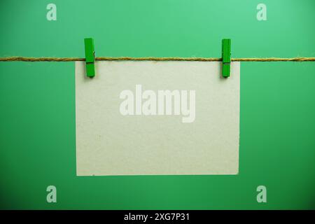 Layout of Empty paper card space for text hanging on the wall with Clothespins on string against green background Stock Photo