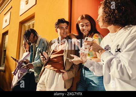 A cheerful group of friends enjoying their time together, sharing moments and fun, while using their smartphones outdoors on a sunny day. Stock Photo
