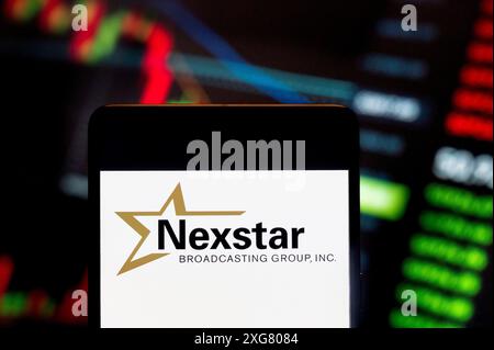 In this photo illustration, the American media company, Nexstar Media Group (NASDAQ: NXST), logo seen displayed on a smartphone with an economic stock exchange index graph in the background. Stock Photo