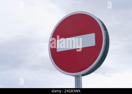 Red circular no entry road sign against a cloudy sky, depicting prohibited or restricted access area. Stock Photo