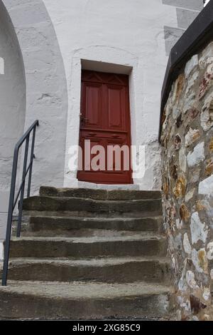 A close-up view of a stone staircase leading to a red wooden door in a whitewashed building Stock Photo
