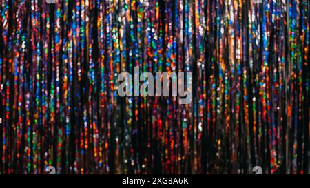 Festive tinsel texture. Bokeh light. Holiday party decor. Defocused red purple blue green orange neon color rainbow curtain glow sparkle blur circles pattern abstract background. Stock Photo