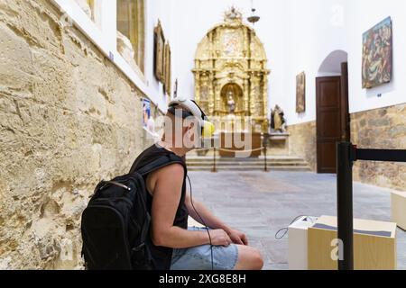 Astorga, Spain - June 4, 2023: A man wearing a VR headset sits in a museum, experiencing virtual reality. The museum is in the Cathedral of Santa Mara Stock Photo