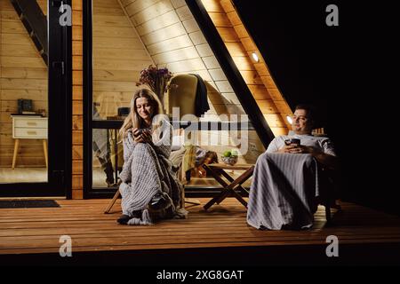 A friendly married couple is sitting on the terrace of log cabin and enjoys warm evening Stock Photo