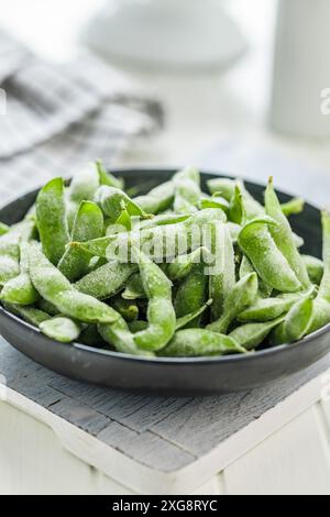Green edamame pods. Fresh soybeans in plate on a white cutting board. Stock Photo